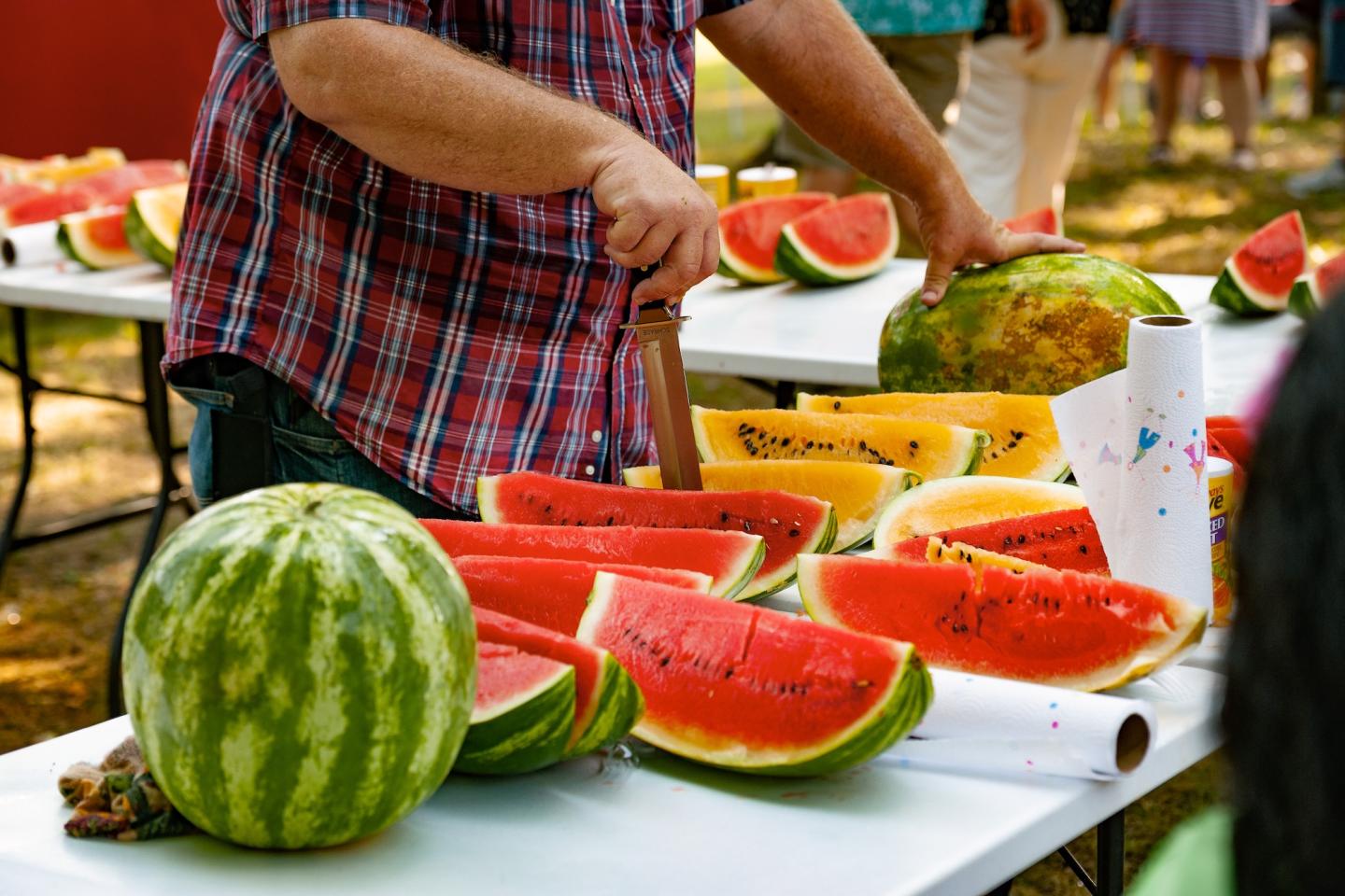 Man slicing watermelons on tables at an outdoor event.