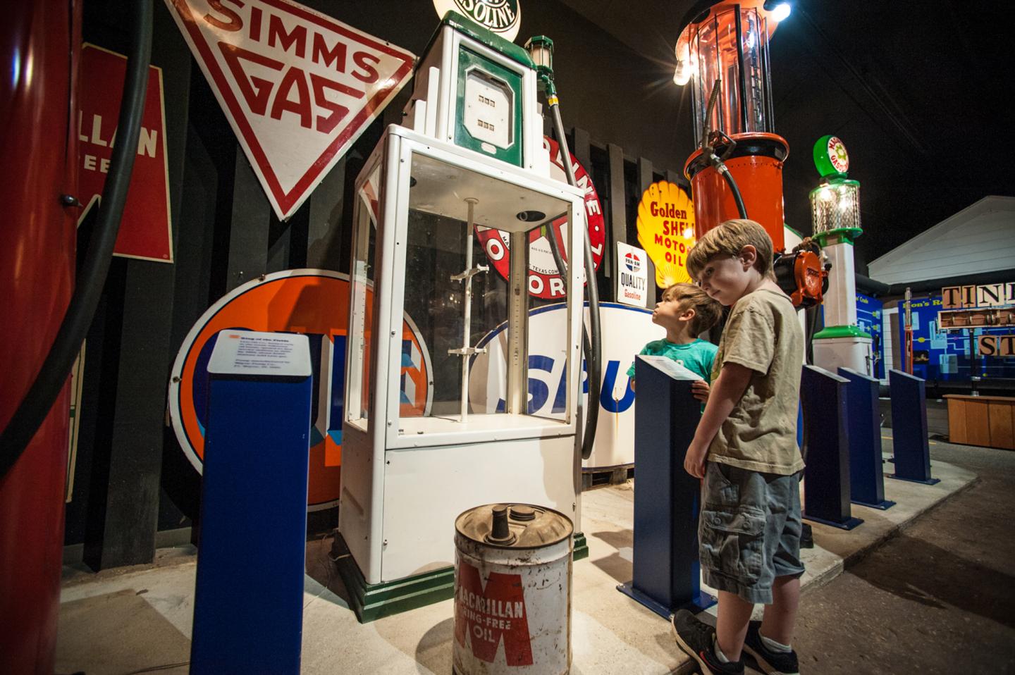 Two children examining a display of vintage gas station signs and pumps.