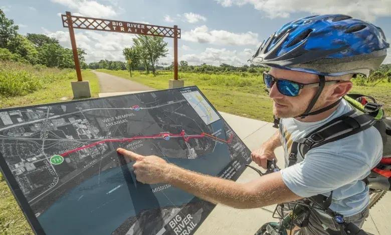 Cyclist pointing at a trail map on a sunny day.