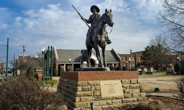 Equestrian statue on brick base in a park setting, clear blue sky above.