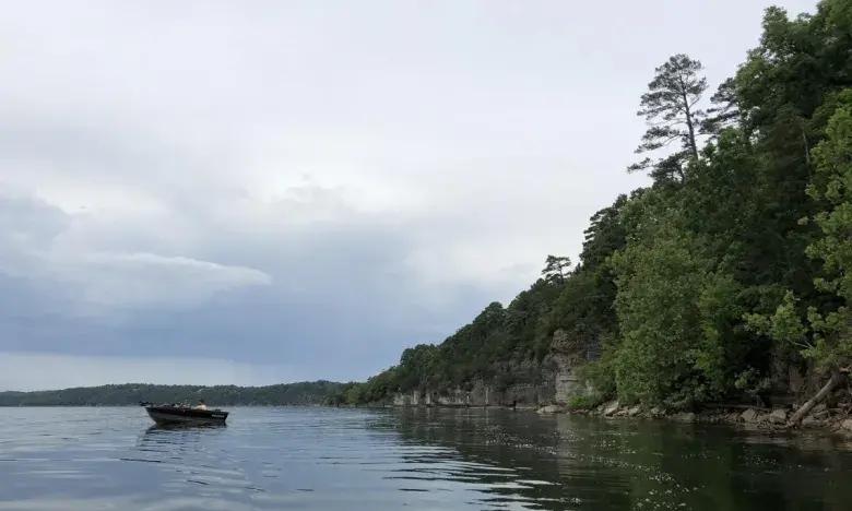 Boat on a calm lake, cloudy sky, lush green shoreline.