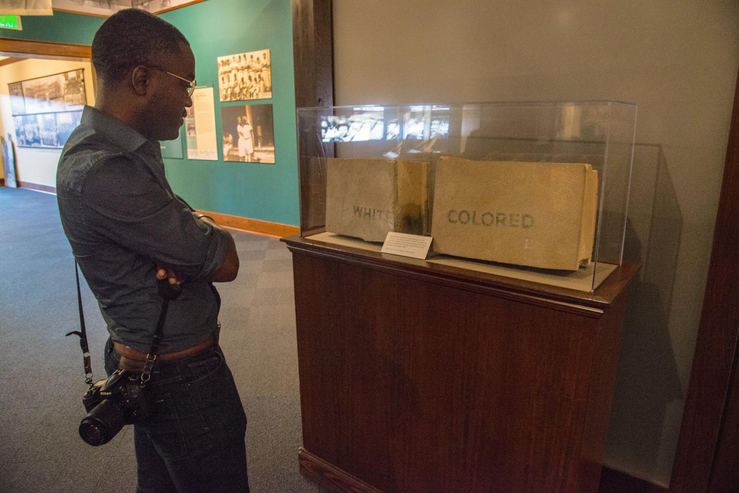 Man examining historical "Colored" sign in museum display case.