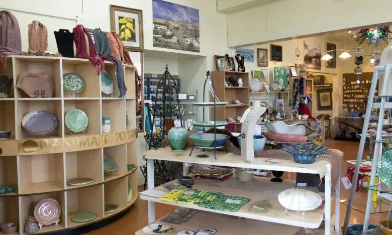 Ceramic shop interior with shelves of pottery and plates, art on walls.