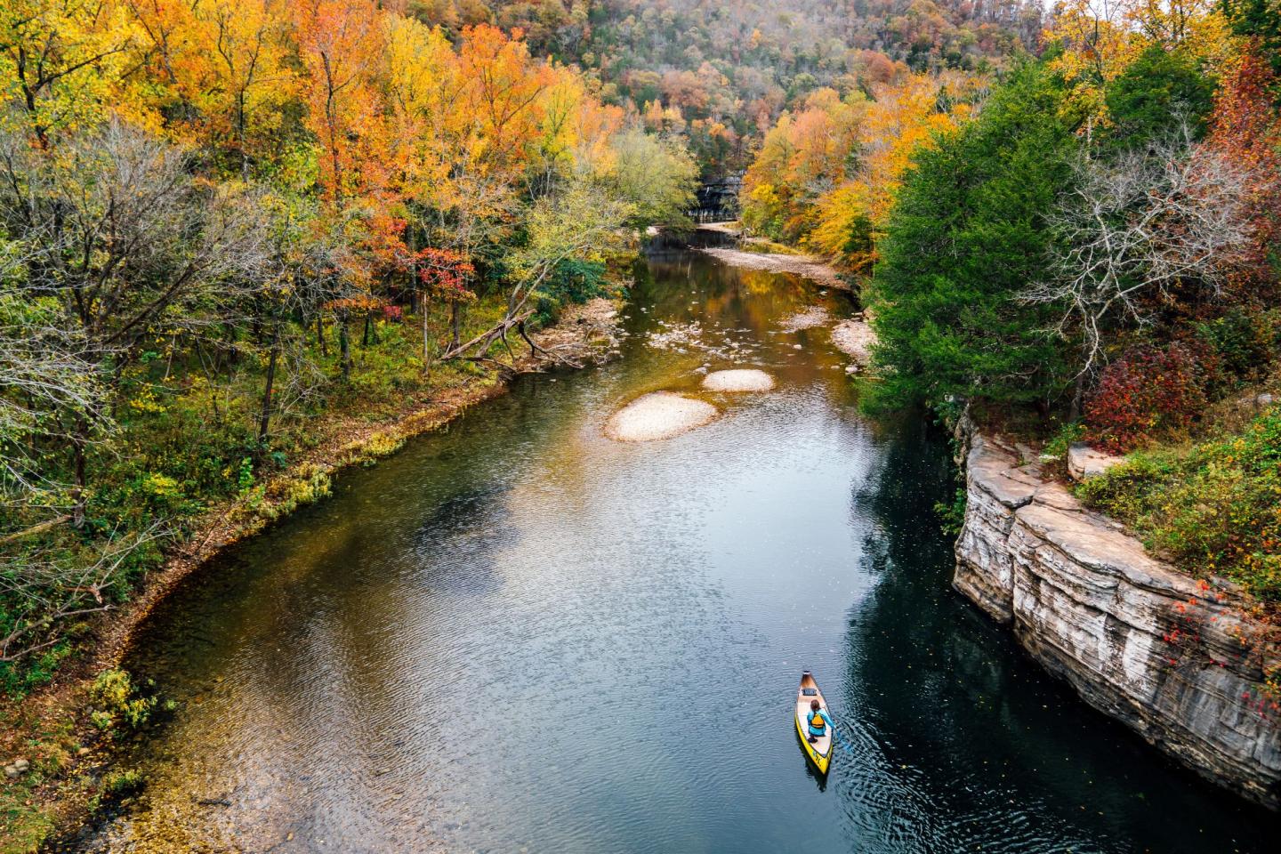 Kayaker on a river surrounded by vibrant autumn trees.