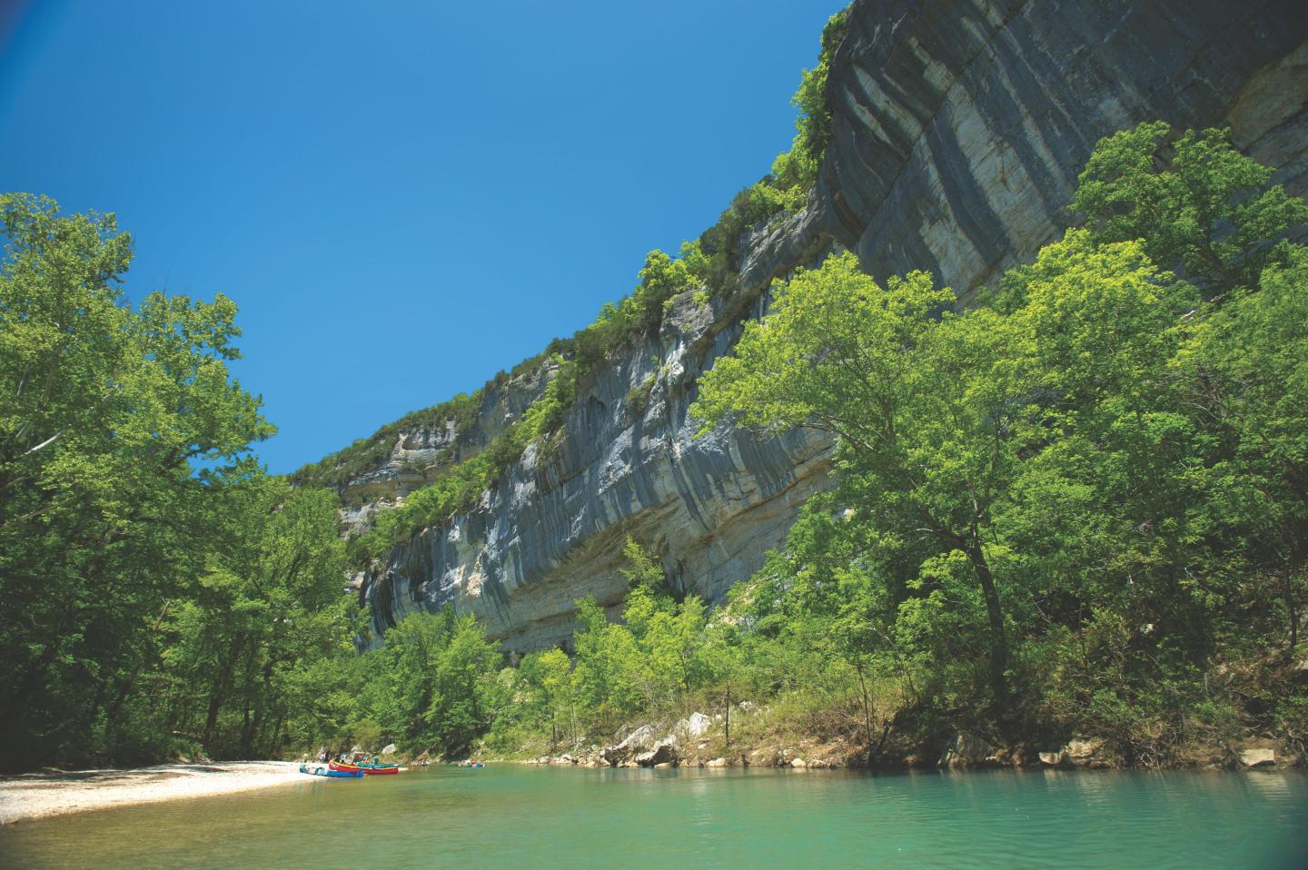 Cliffside view with trees and a turquoise river under a clear blue sky.