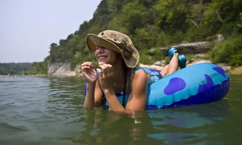 Woman in hat smiling while floating on blue tube in a lake.