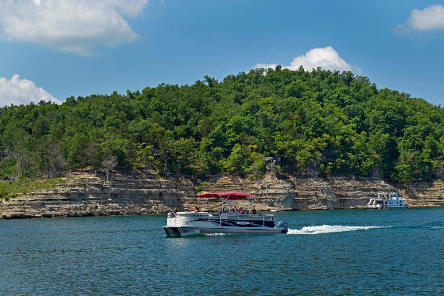 Boat cruising on a lake with a forested hill in the background.