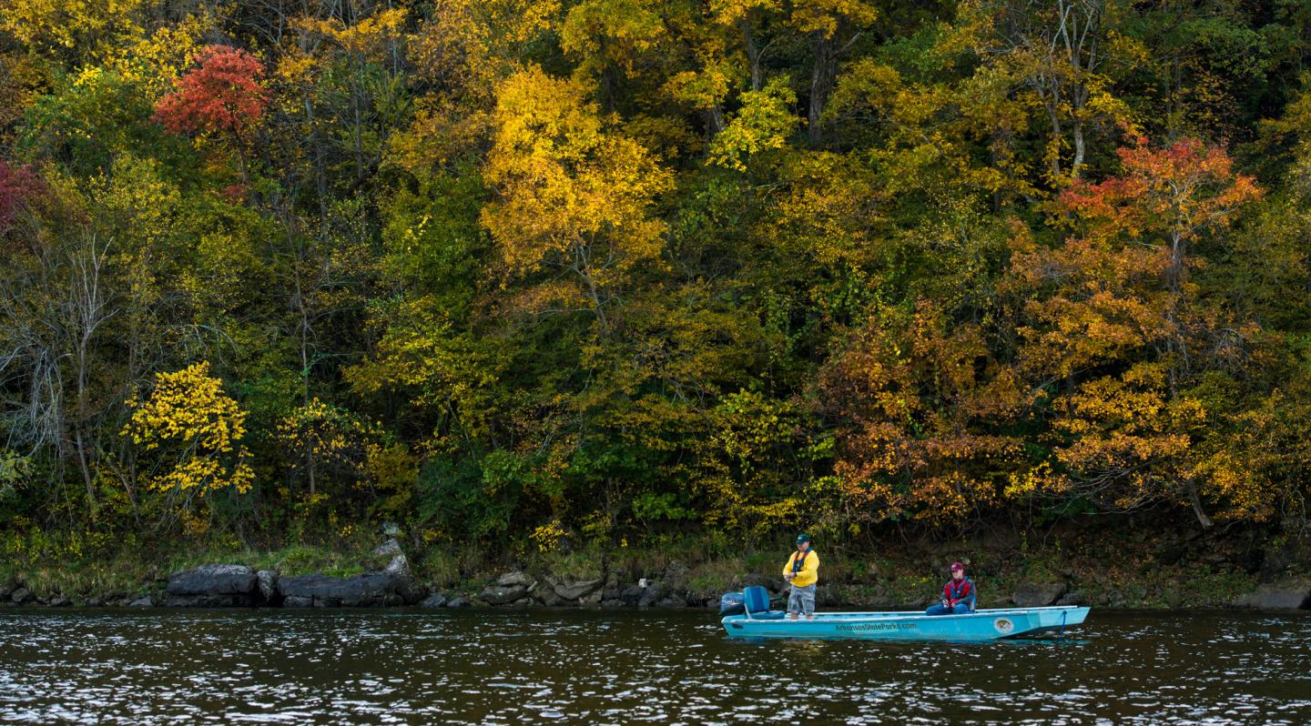 Boat with two people on a lake, surrounded by vibrant autumn trees.