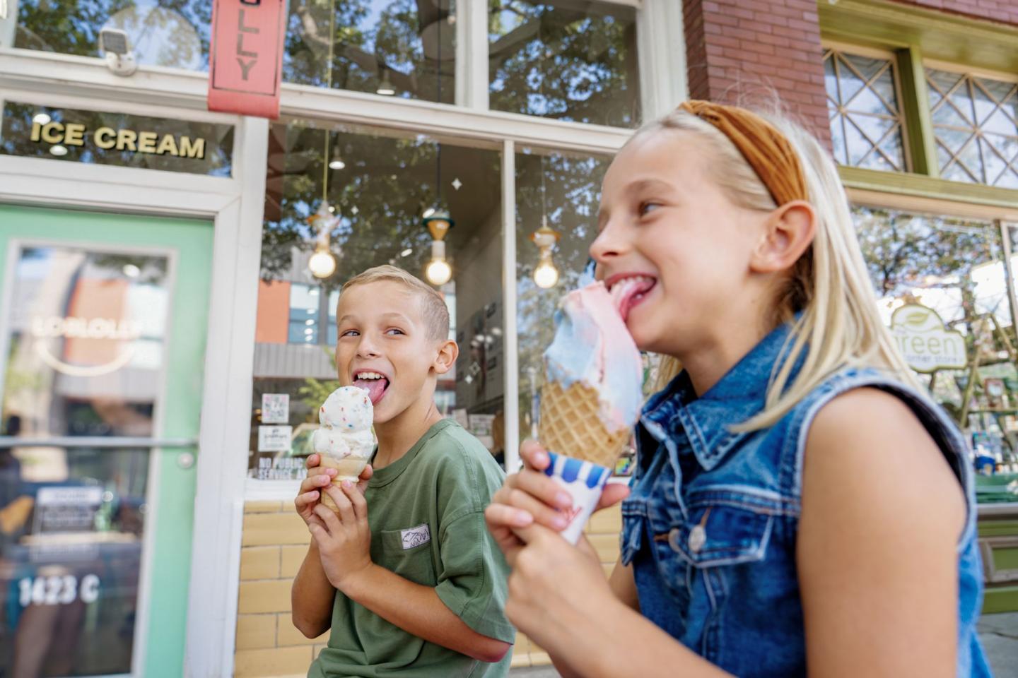 Kids happily eating ice cream cones outside a shop.