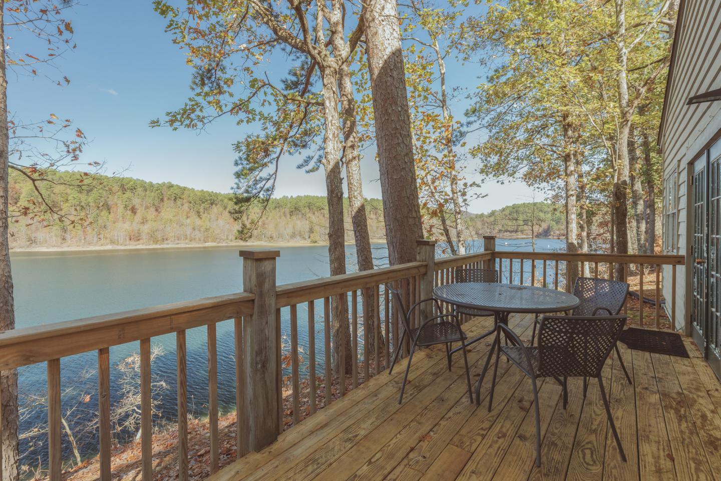 Lake view from a wooden deck with a table and chairs, surrounded by trees.