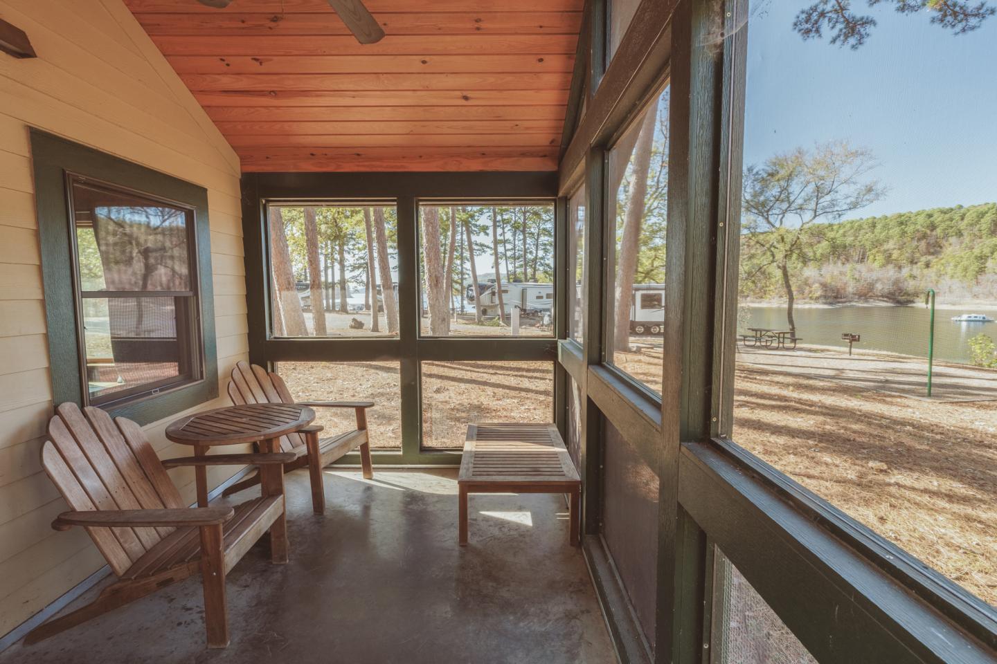 Wooden porch with chairs, table, and lake view through screened windows.
