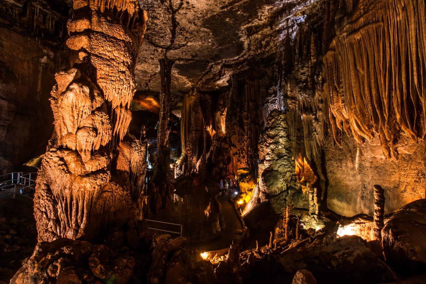 Dimly lit cave with stalactites and stalagmites, featuring warm earthy colors.