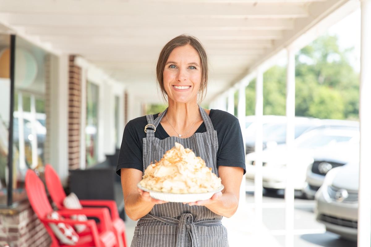 Woman smiling, holding a plate of meringues outside a shop.