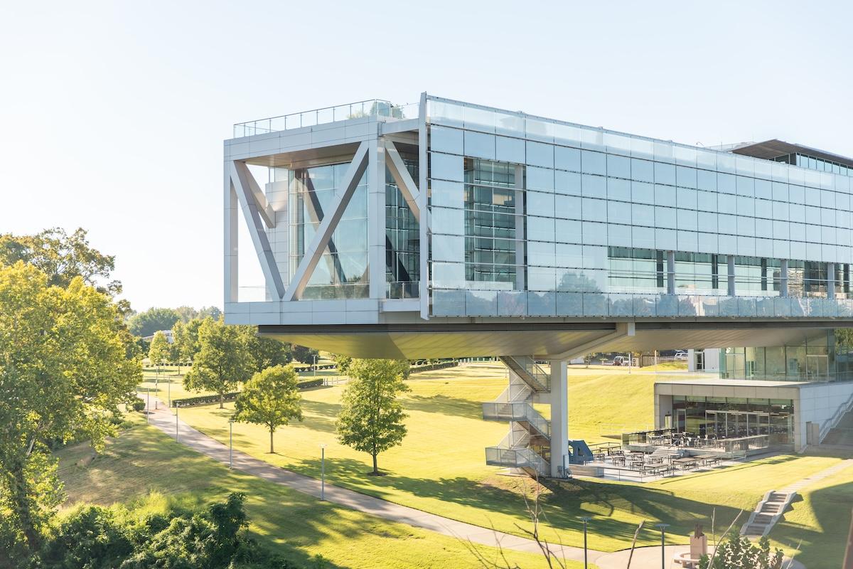Modern glass building on stilts in a sunny park setting.
