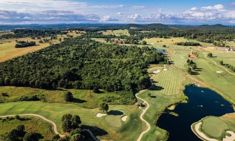 Aerial view of a golf course with trees and a small lake under a blue sky.