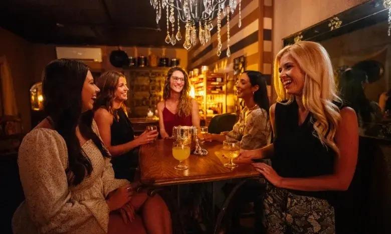 Women socializing at a dimly lit bar with drinks.