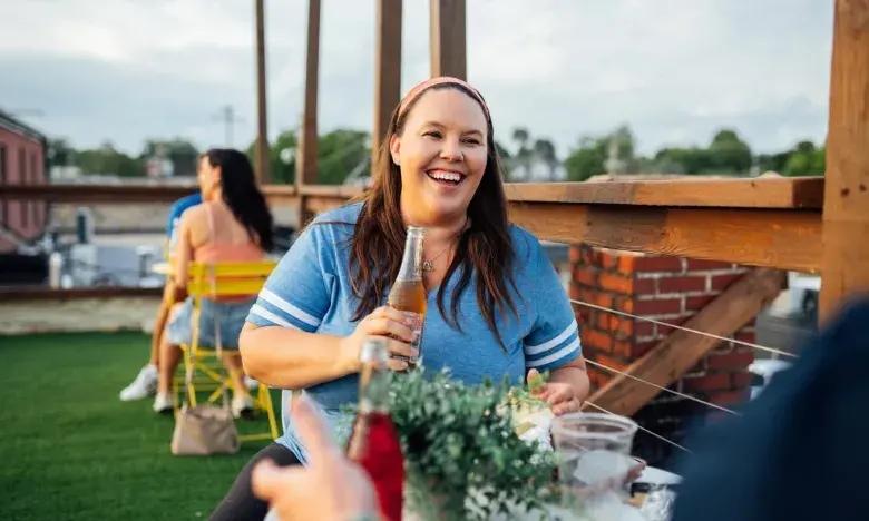 Woman smiling with a drink on a rooftop terrace, summer evening.