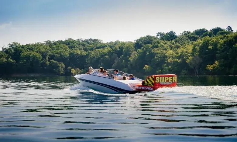 Speedboat gliding on a lake near a forested shore, under a clear sky.