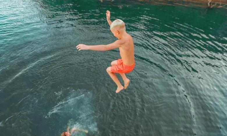 Boy in orange shorts jumps into a lake.