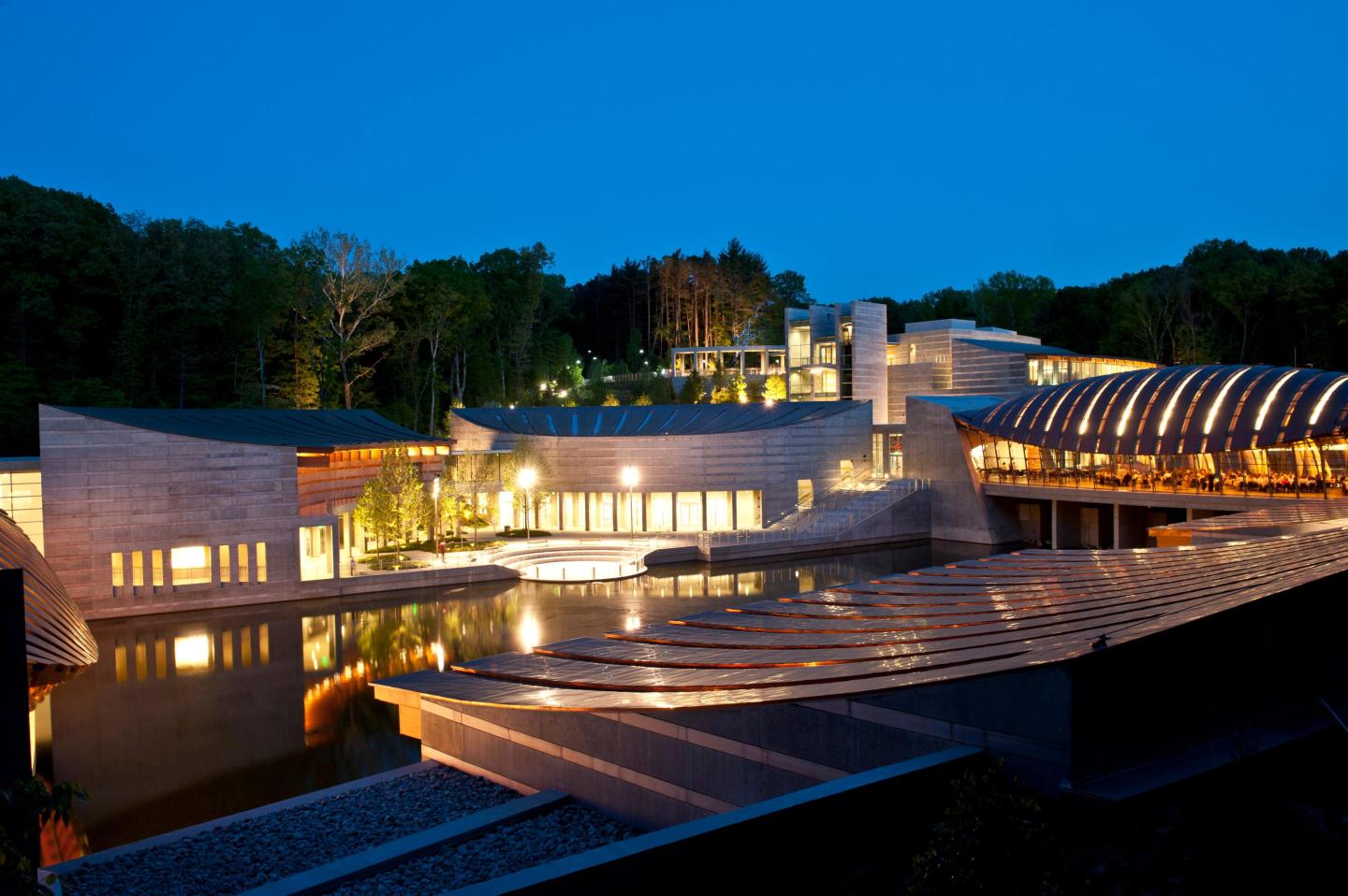 Modern building with illuminated windows, set against a night sky with trees.