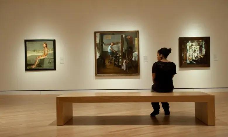 Sitting person in art gallery viewing three paintings on the wall.