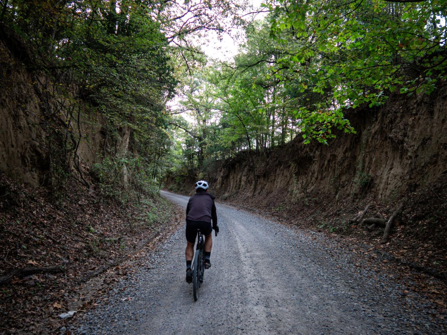 Cyclist on a gravel path between wooded hills.