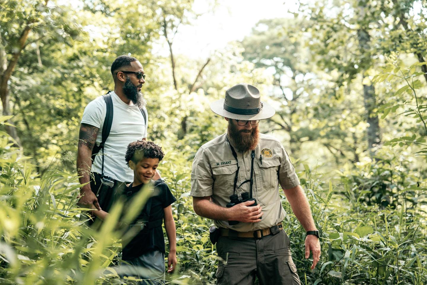 Park ranger guiding man and child through lush forest.