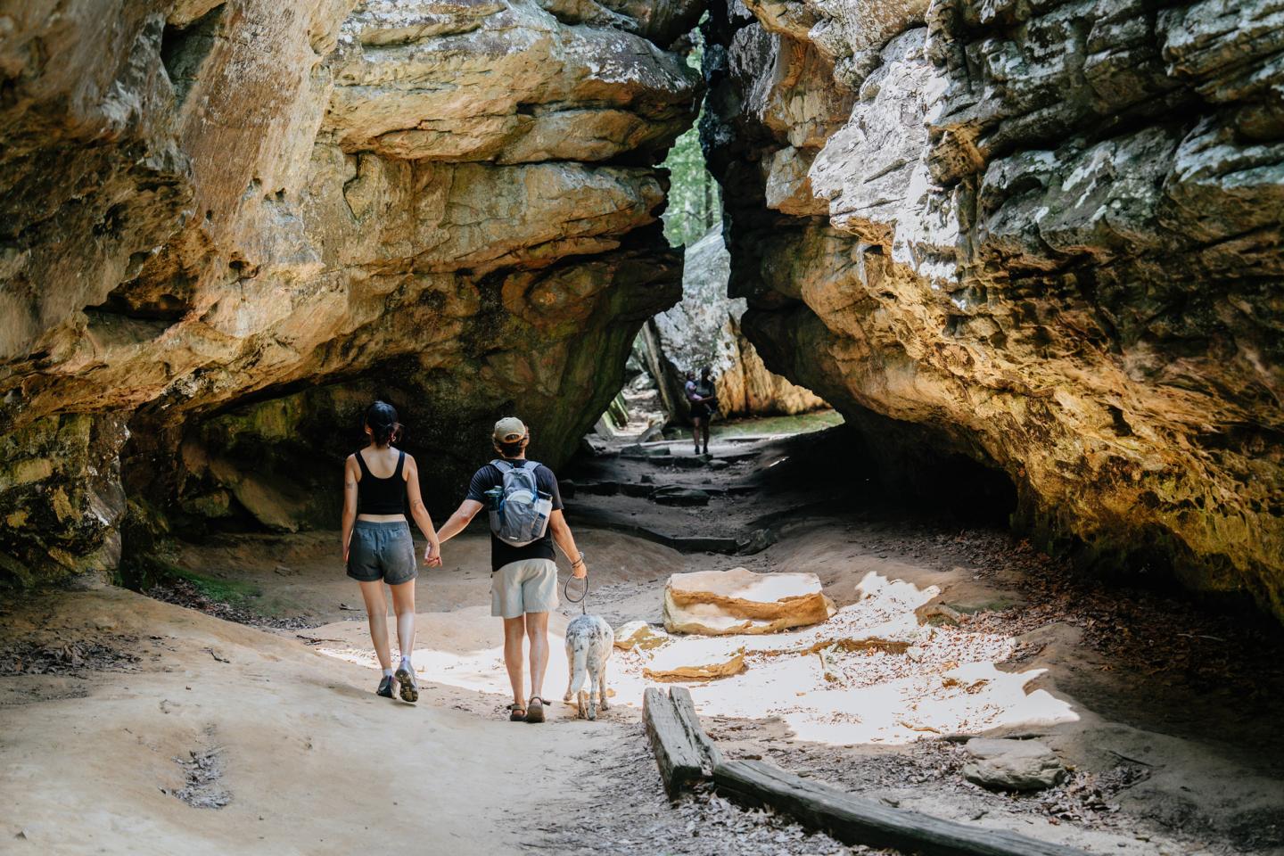 Couple and dog hiking through rocky canyon walkway.