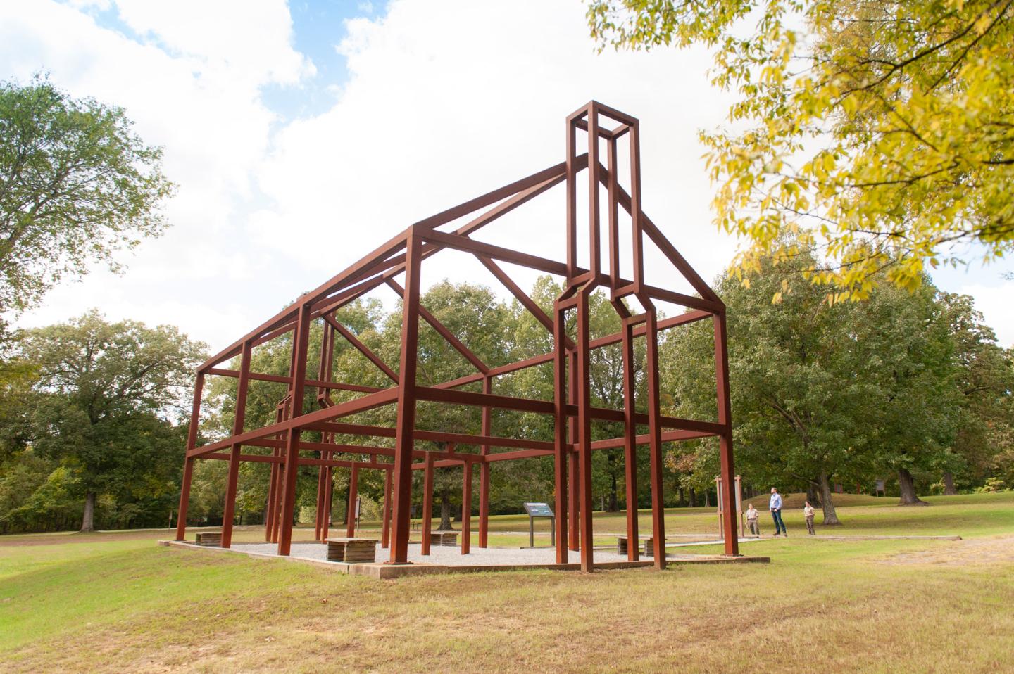 Rustic metal structure resembling a house frame in a park setting.