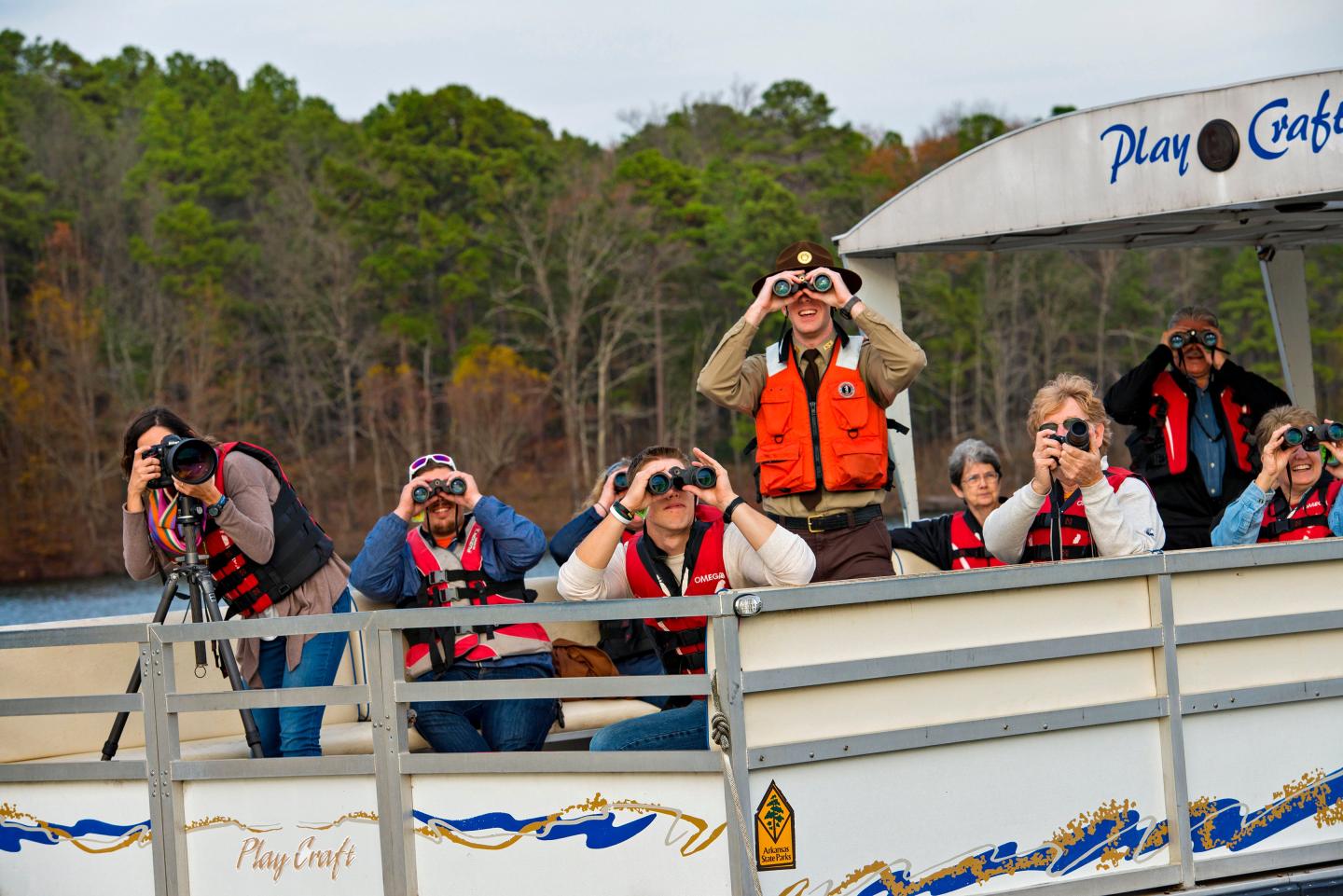 People on a boat using binoculars on a lake, wearing life jackets.