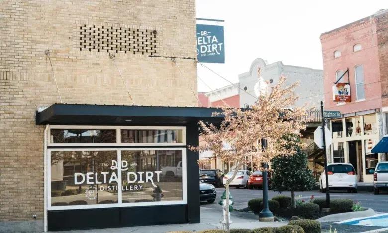 Storefront on a sunny street with a sign reading "Delta Dirt Distillery."