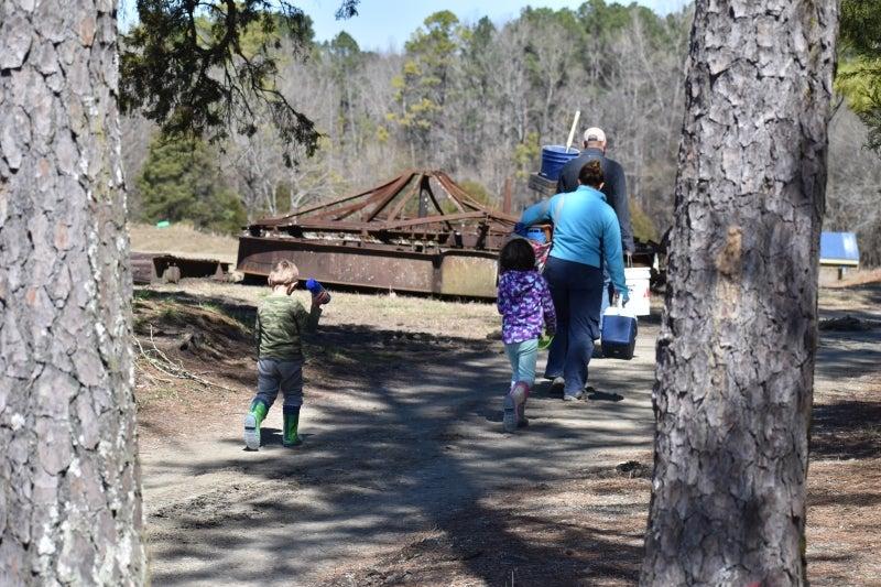Family walking on a path in a park, surrounded by trees and sunlight.