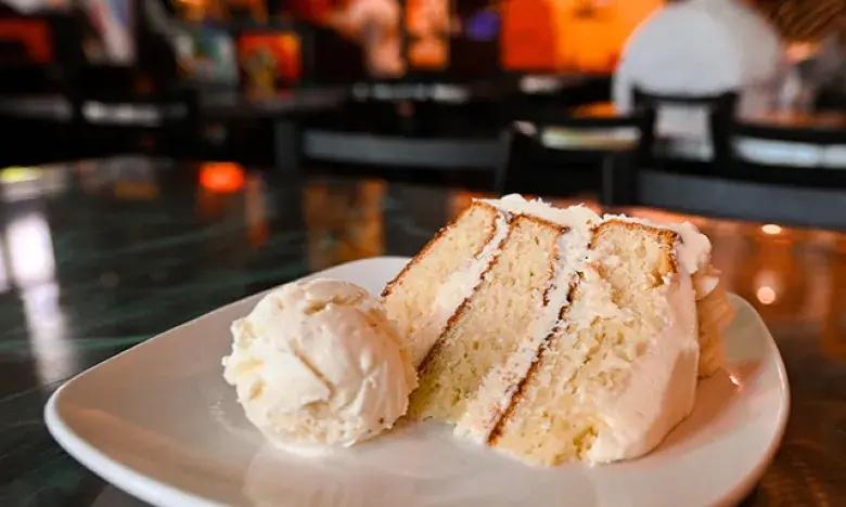 Cake slice with icing and ice cream on a plate in a dimly lit restaurant.
