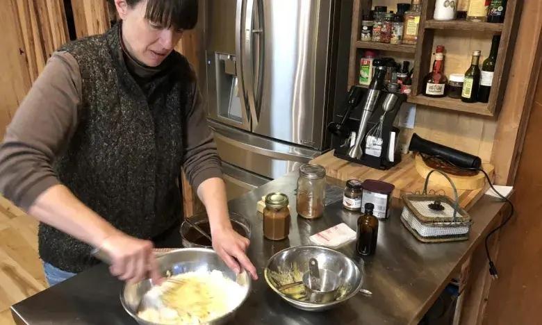 Woman mixing ingredients in a kitchen with jars on the counter.