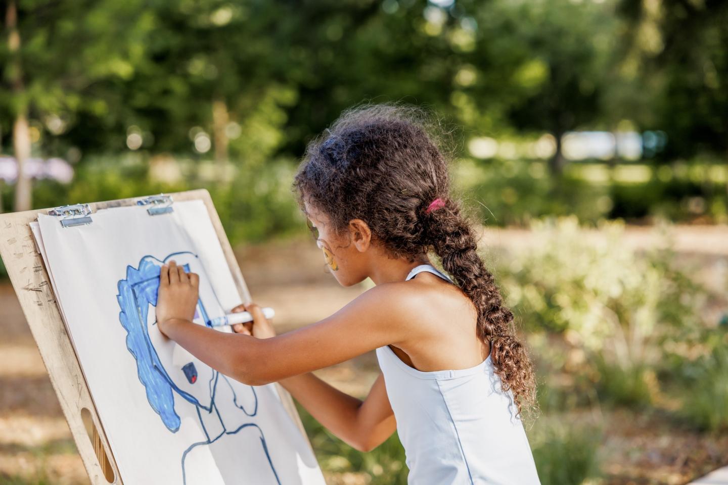 Child painting on an easel in a sunny park.