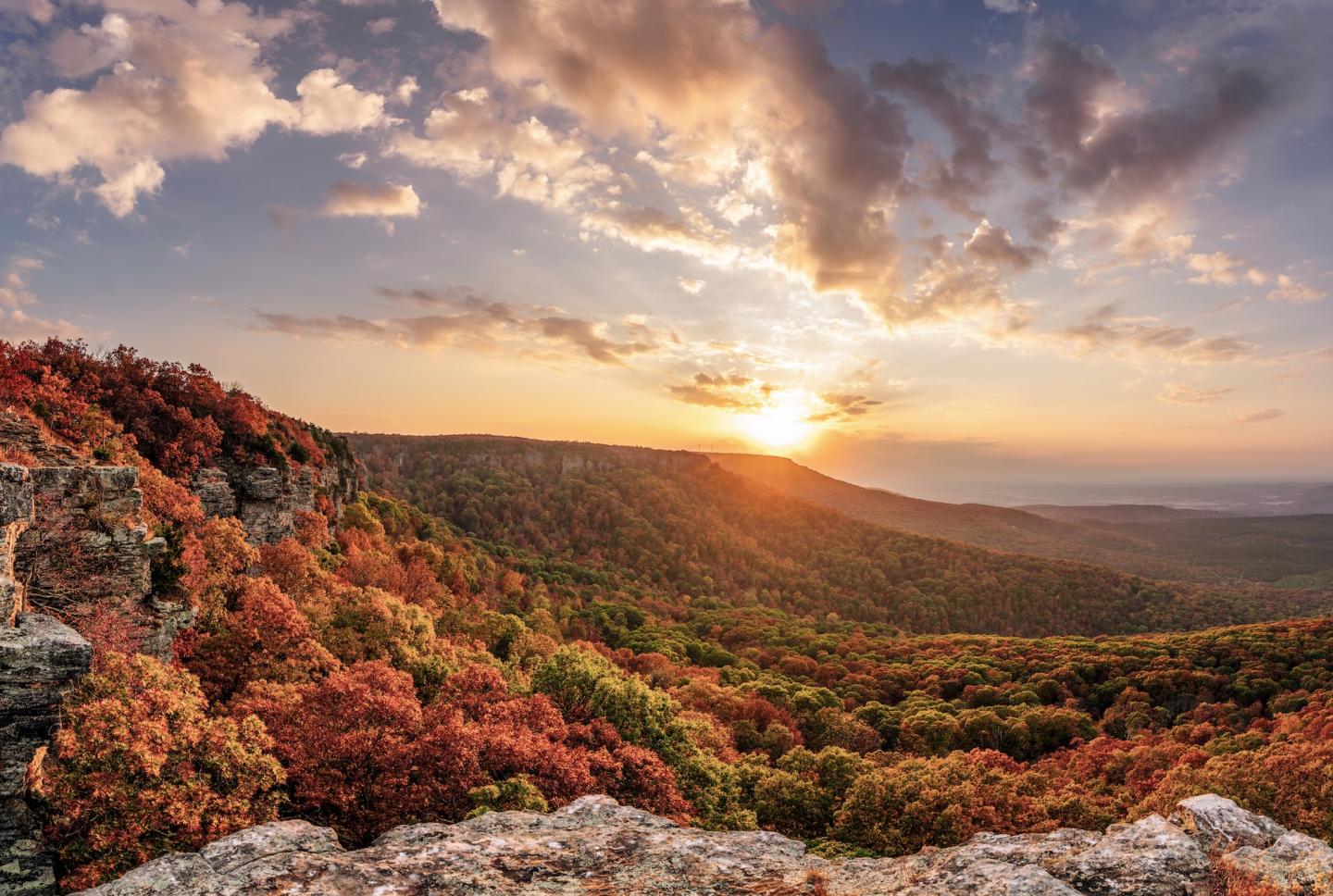Sunset over a forest with autumn colors and rocky cliffs.