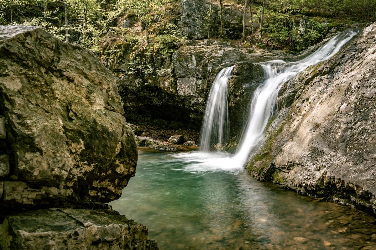 Waterfall flowing into a turquoise pool surrounded by rocky cliffs and greenery.