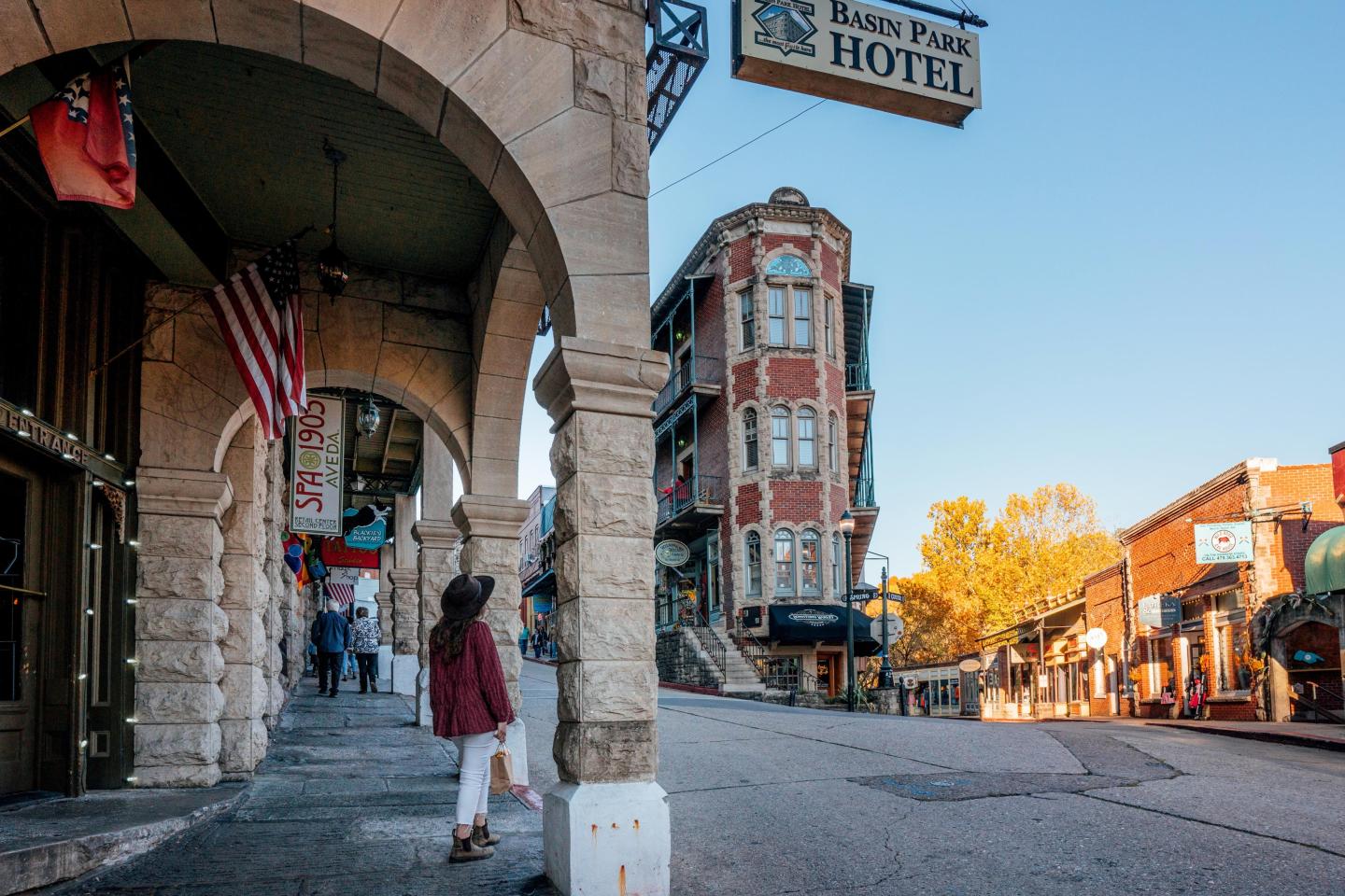 Historic street scene with autumn trees, a hotel sign, and person walking under arches.
