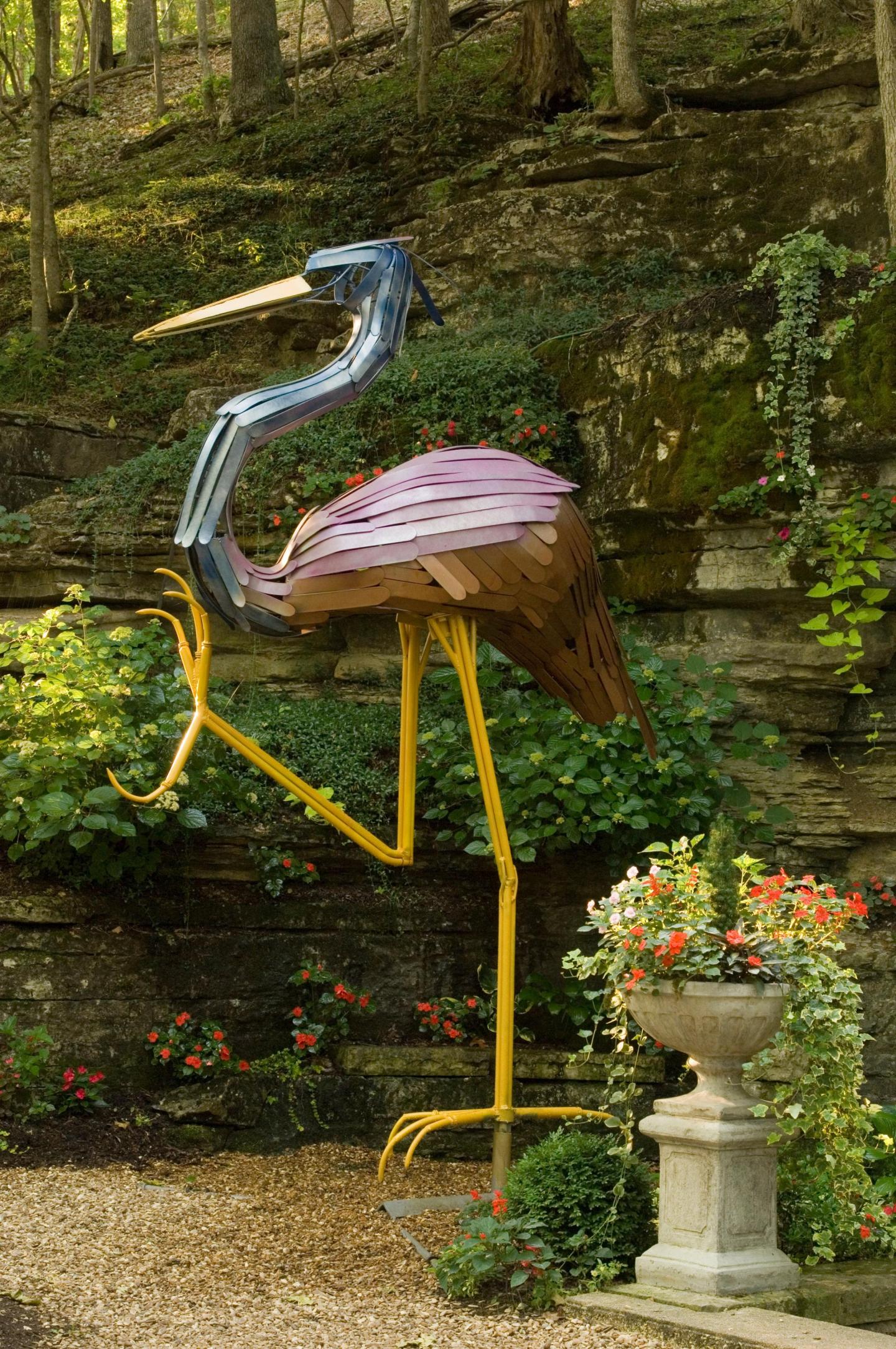 Colorful heron sculpture in a garden with greenery and flowers.
