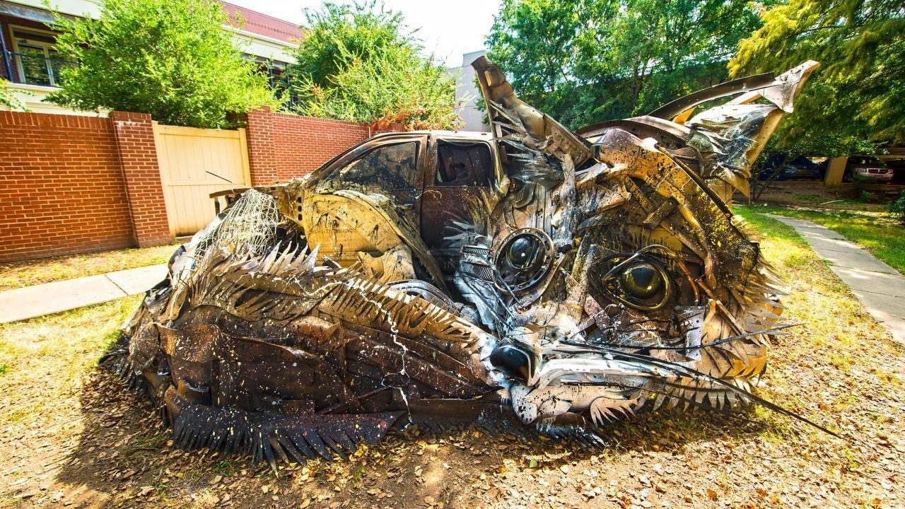 Large metal sculpture of a reclining cat in an outdoor garden setting.