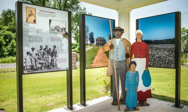 Three mannequins in period clothing stand between historical display panels.