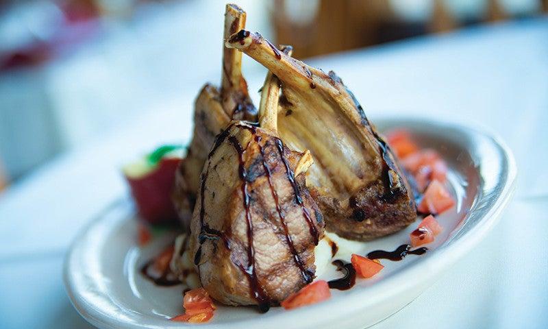 Grilled lamb chops with sauce and diced tomatoes on a white plate.