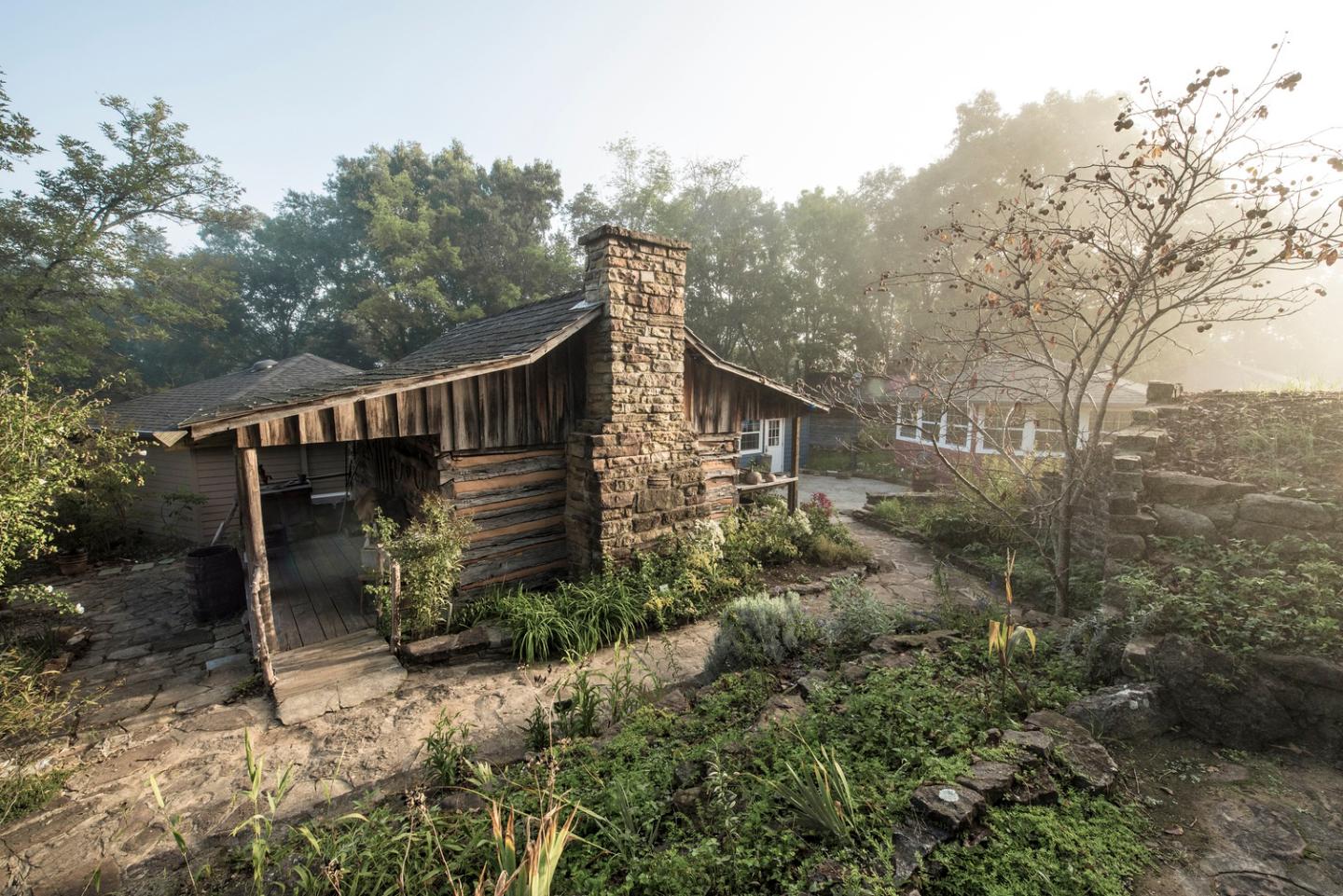 Rustic cabin with stone chimney in a lush, green garden.