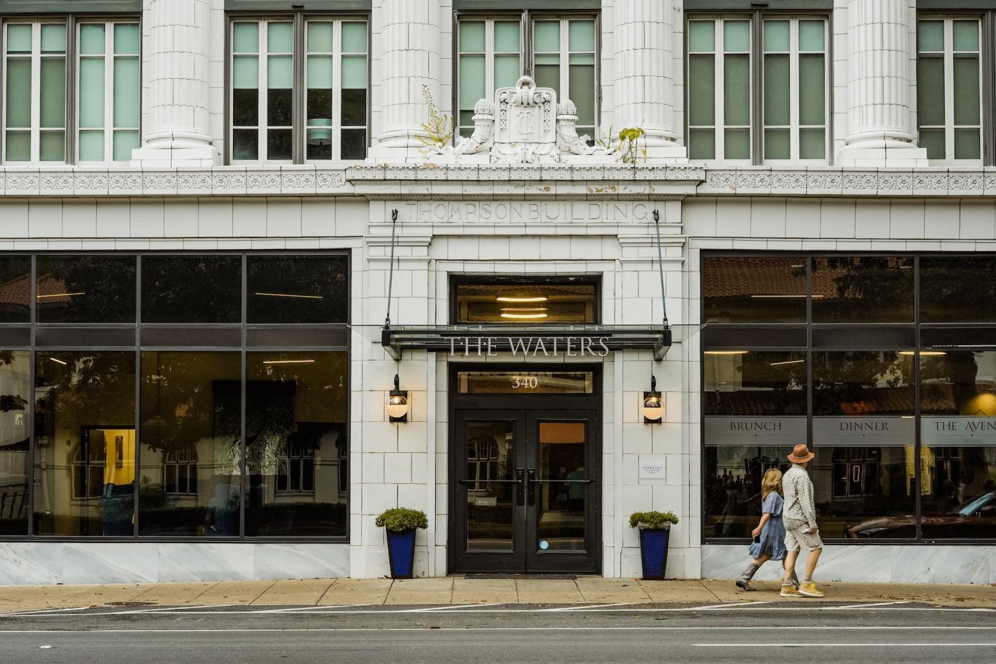 Elegant white building facade with large windows and two people walking past.