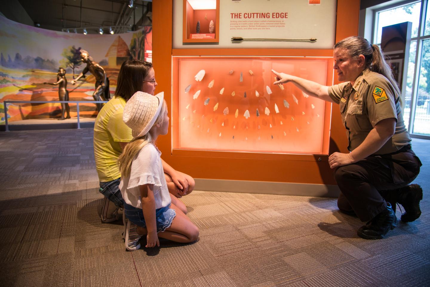 A ranger explaining an exhibit to two children in a museum.