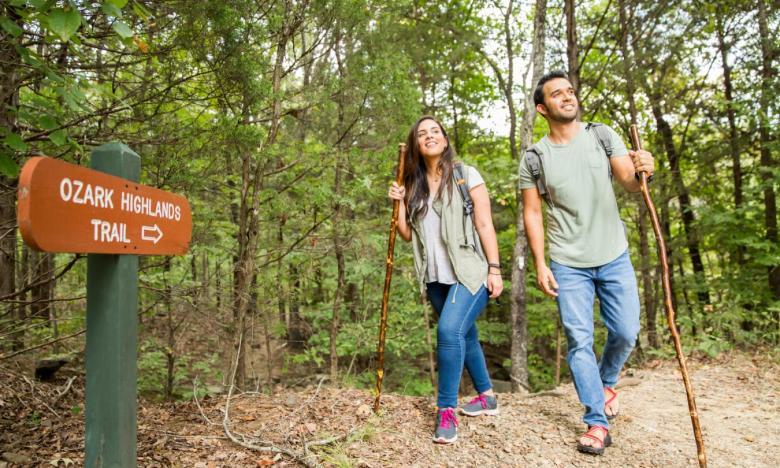 Two people hiking in a wooded trail with walking sticks.