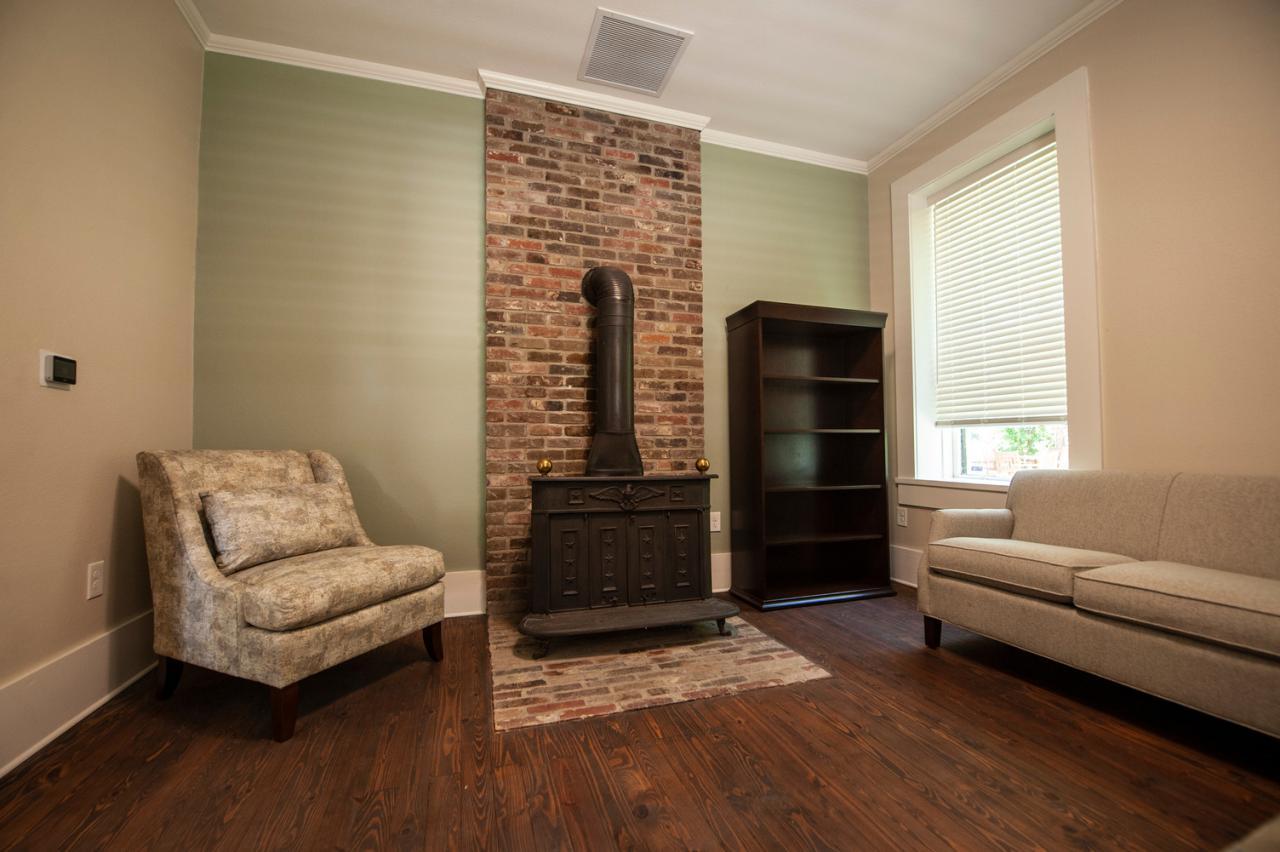 Cozy room with fireplace, armchair, sofa, and bookshelf on wooden floor.