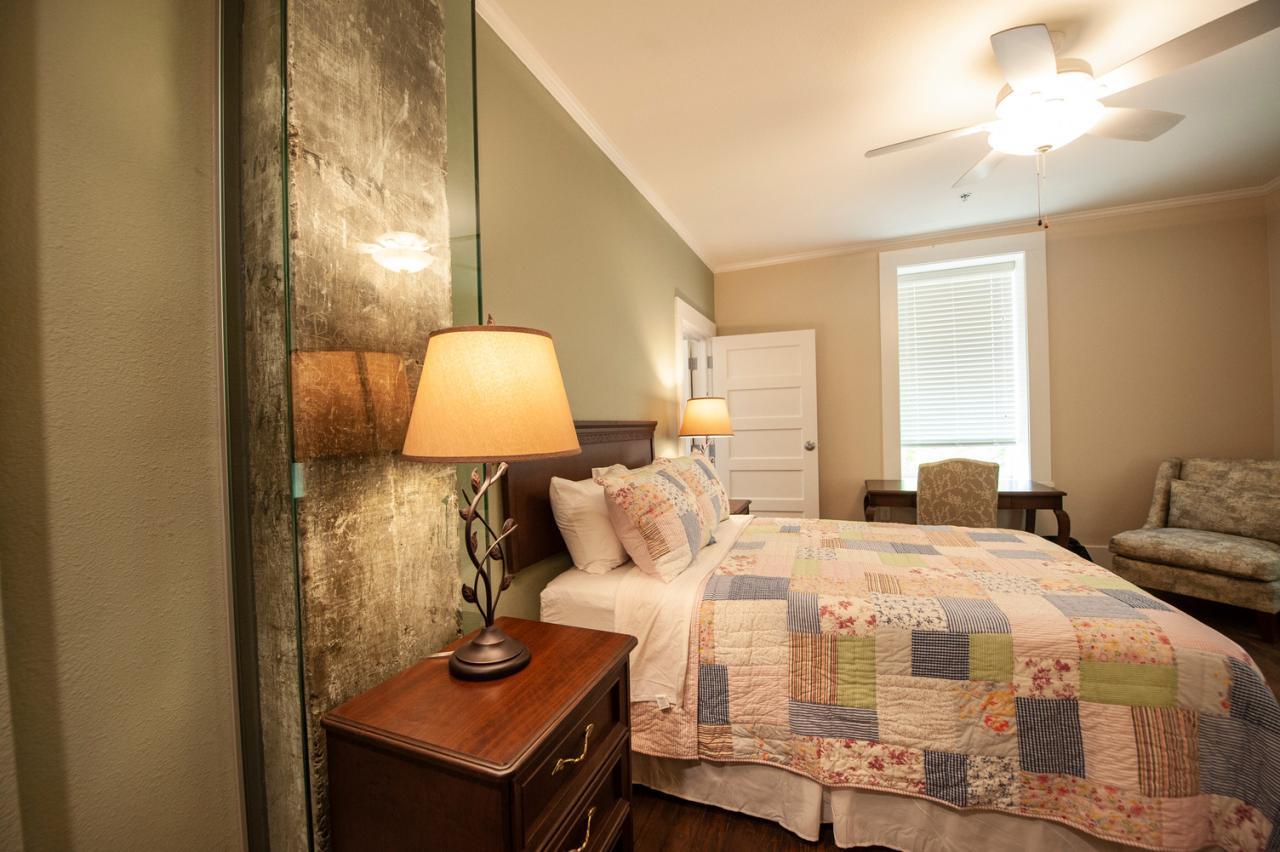 Cozy bedroom with a quilted bed, lamp, window, and armchair.