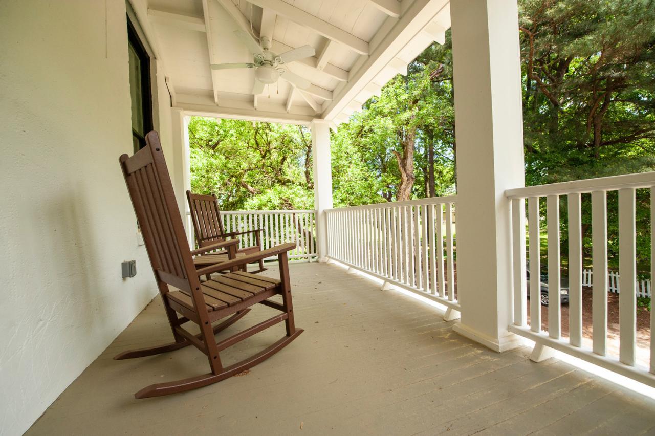 Two wooden rocking chairs on a spacious porch overlooking green trees.