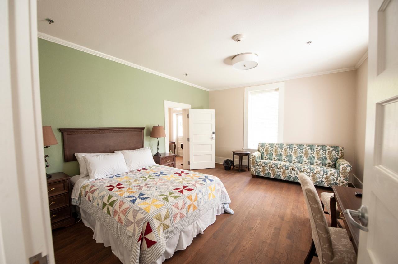 Bedroom with pastel walls, patterned bedspread, sofa, and wooden floor.